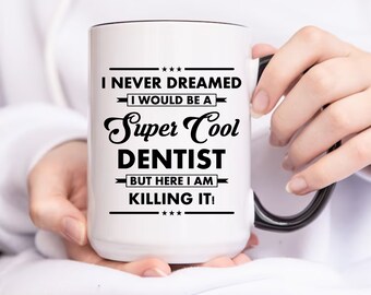 May include: White ceramic mug with a black handle. The mug has black text that reads "I never dreamed I would be a Super Cool Dentist but here I am killing it!"