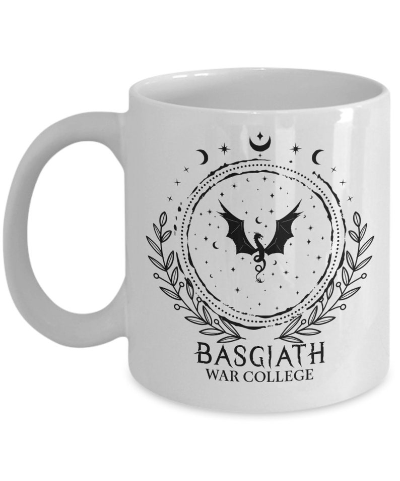 May include: White ceramic mug featuring a black dragon design within a circular frame of stars, moons, and leaves. The text "BASGIATH WAR COLLEGE" is printed below the design. The mug has a curved handle.