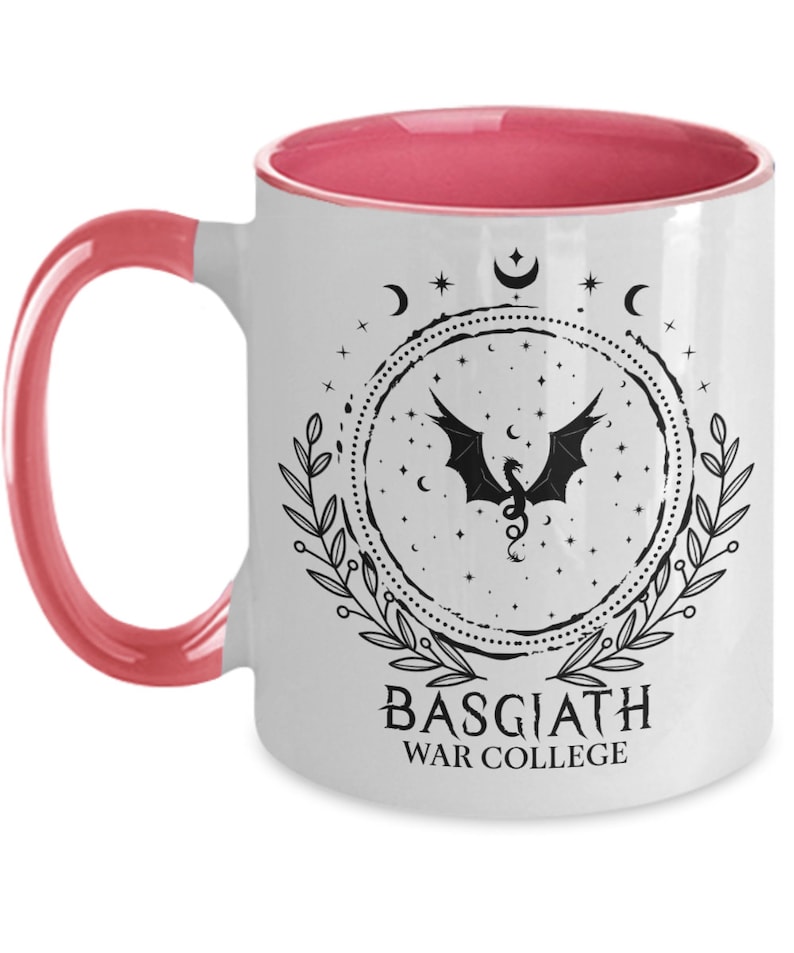 May include: White ceramic mug with a pink interior and handle. The mug features a black dragon design within a circular frame, surrounded by stars, moons, and leaves. The text "BASGIATH WAR COLLEGE" is printed below the design.