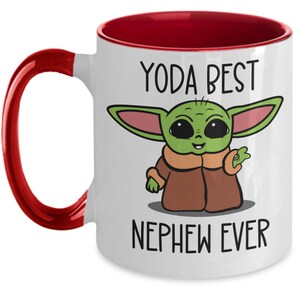 May include: White ceramic coffee mug with a red rim and handle. The mug features a cartoon image of a green Baby Yoda character with the text "Yoda Best Nephew Ever".