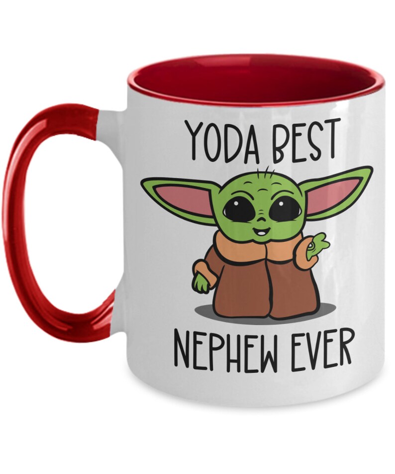 May include: White ceramic coffee mug with a red rim and handle. The mug features a cartoon image of a green Baby Yoda character with the text "Yoda Best Nephew Ever".