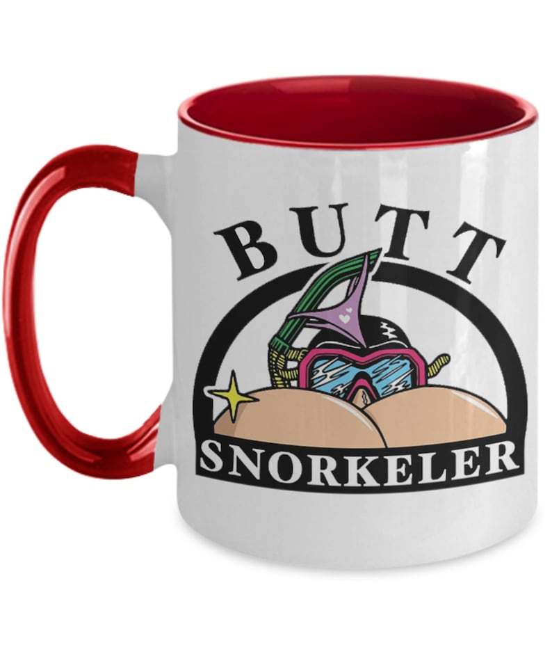 May include: White ceramic mug with a red interior and handle. The mug features the words "BUTT SNORKELER" in black, with a cartoon illustration of a snorkel mask and bikini bottoms.