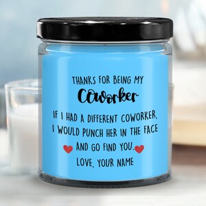 May include: A blue glass candle jar with a black lid. The label reads "Thanks for being my coworker. If I had a different coworker, I would punch her in the face and go find you. Love, your name."