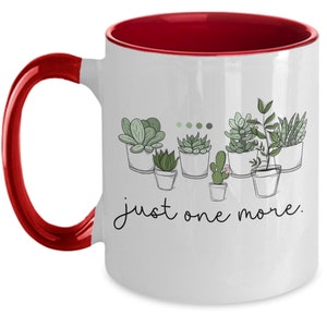 May include: White ceramic coffee mug with a red rim and handle. The mug features a line drawing of potted succulents with the text "just one more."
