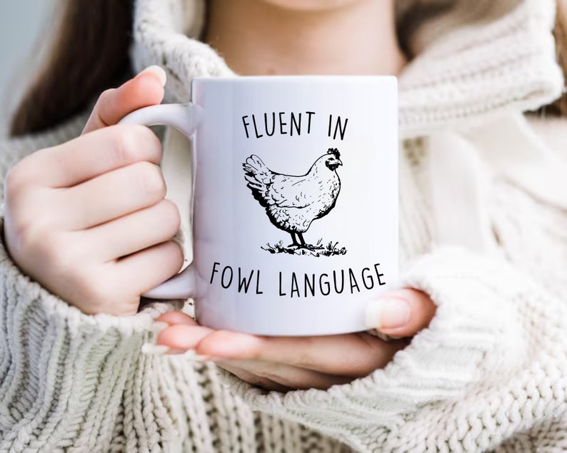 May include: White ceramic mug with a black and white illustration of a chicken and the text "Fluent in Fowl Language".