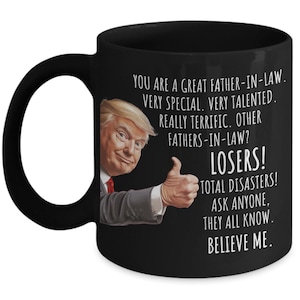 Puede incluir: Taza de cerámica negra con interior blanco y asa negra grande. La taza presenta un retrato de un hombre haciendo una señal de aprobación, con el texto: «YOU ARE A GREAT FATHER-IN-LAW. LOSERS! BELIEVE ME.»