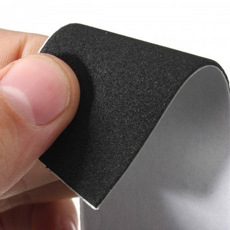 May include: A close-up of a piece of black, textured material with a white edge, held by a person. The material has a rough, grainy surface and a smooth, gray underside. The focus is on the texture and contrast of the materials.