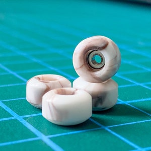 May include: Four brown and white marble skateboard wheels stacked on top of each other. The wheels are on a green gridded surface.