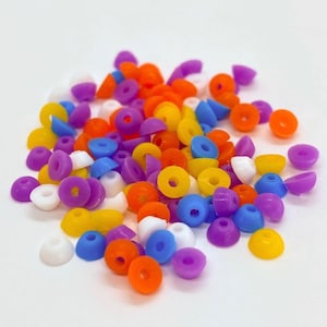 Puede incluir: Una colección de cuentas de plástico de colores en varios tonos de morado, azul, amarillo, naranja y blanco. Las cuentas tienen forma de pequeñas rosquillas planas con un agujero en el centro.