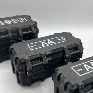 Könnte beinhalten: Drei schwarze Kunststoff-Aufbewahrungsboxen mit unterschiedlichen Etiketten. Die erste Box ist mit "18650+" beschriftet, die zweite Box mit "AA+" und die dritte Box mit "AA+".