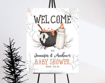 May include: Welcome to Jennifer & Andrew's Baby Shower sign featuring a black cauldron, orange liquid, and a baby bottle. The sign has a spiderweb design and the text "Welcome to Jennifer & Andrew's Baby Shower 20XX.09.03"