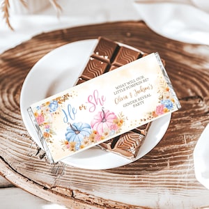 May include: A chocolate bar with a decorative wrapper, featuring the text "He or She" and "What will our little pumpkin be? Olivia & Jackson's Gender Reveal Party." The wrapper has illustrations of blue and pink pumpkins with floral accents.