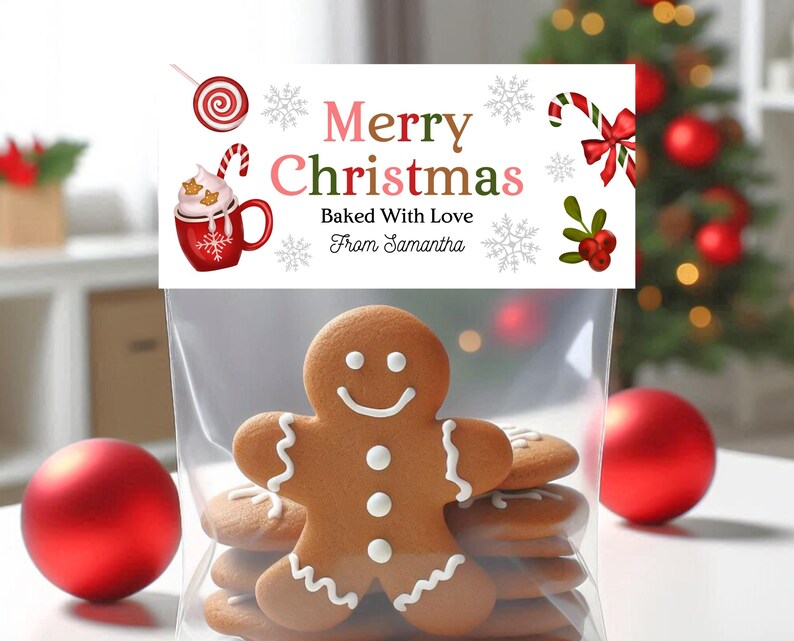 May include: A clear cellophane bag filled with gingerbread cookies, including a smiling gingerbread man. The bag has a decorative tag that reads "Merry Christmas Baked With Love From Samantha" with festive illustrations of a candy cane, snowflakes, and a mug of hot cocoa.