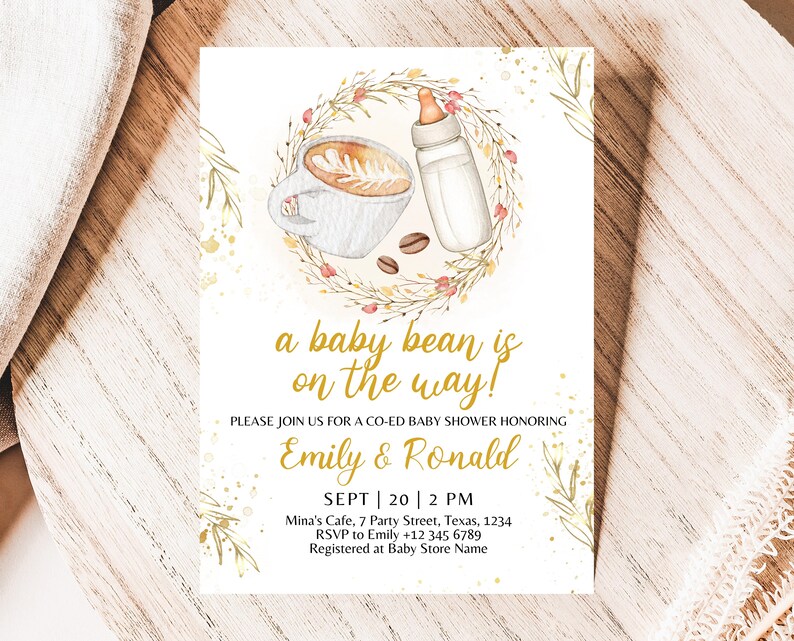K&ouml;nnte beinhalten: Eine Babyparty-Einladung mit einer Aquarell-Illustration einer Tasse Kaffee und einer Babyflasche, umgeben von einem Kranz aus Bl&auml;ttern und Blumen. Der Text lautet "a baby bean is on the way!" und enth&auml;lt die Namen "Emily & Ronald", das Datum "SEPT | 20 | 2 PM", den Ort "Mina's Cafe, 7 Party Street, Texas, 1234" und die RSVP-Informationen "RSVP to Emily +12 345 6789".