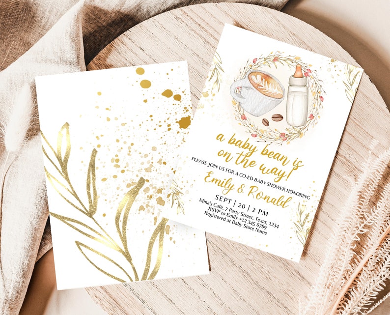 K&ouml;nnte beinhalten: Eine wei&szlig;e Babyparty-Einladung mit goldenen Akzenten. Die Einladung zeigt eine Kaffeetasse und eine Babyflasche mit einem Kranz aus Bl&auml;ttern und Blumen. Der Text lautet "a baby bean is on the way!" und enth&auml;lt die Namen "Emily & Ronald" sowie das Datum und die Uhrzeit der Party.