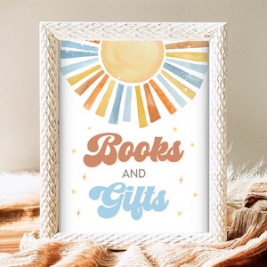 May include: A white framed print with a watercolor sun design and the text "Books and Gifts" in a retro font.