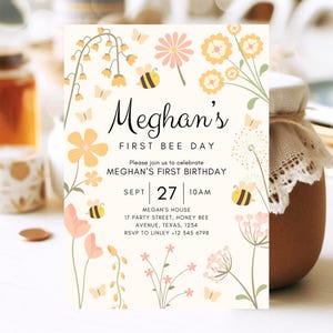 May include: A yellow and white bee-themed first birthday invitation with a floral design. The invitation says "Meghan's First Bee Day" and includes the date "Sept 27" and time "10 AM".