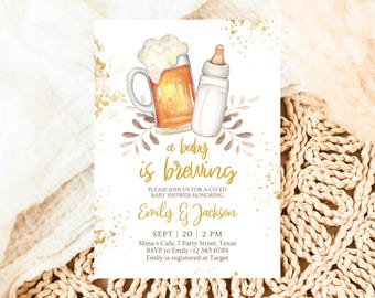 Può includere: Un invito a una festa di benvenuto per un bambino con un design oro e bianco. L'invito presenta una boccale di birra e un biberon con il testo "a baby is brewing". L'invito include anche i nomi "Emily & Jackson" e la data e l'ora della festa.