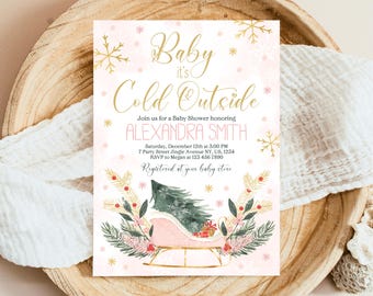 May include: A pink and gold baby shower invitation with a winter theme. The invitation features a pink sleigh with a green pine tree and red berries. The text on the invitation reads "Baby it's Cold Outside" and includes the name "Alexandra Smith".