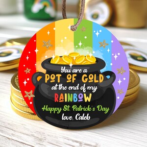 Peut inclure: Une étiquette ronde et colorée avec un fond arc-en-ciel et un pot d'or noir au bout. L'étiquette porte le texte "You are a POT OF GOLD at the end of my RAINBOW Happy St. Patrick's Day love, Caleb".