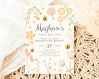 Op de afbeelding: Een witte uitnodigingskaart met een bloemenontwerp en een bijenmotief. De tekst op de kaart luidt "Meghan's First Bee Day" en bevat details voor een eerste verjaardagsfeest.