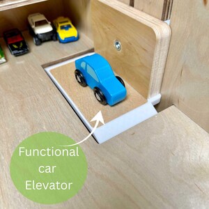 May include: A wooden toy car elevator with a blue toy car on the platform. The elevator is part of a larger wooden toy set, with other toy cars visible in the background. The text "Functional car Elevator" is in a green circle.