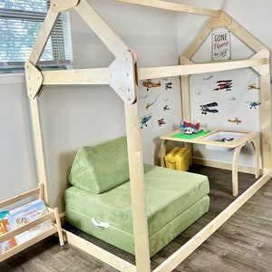 May include: A wooden playhouse frame with a green cushioned seat inside. The playhouse has a sign that says "Gone Flying".