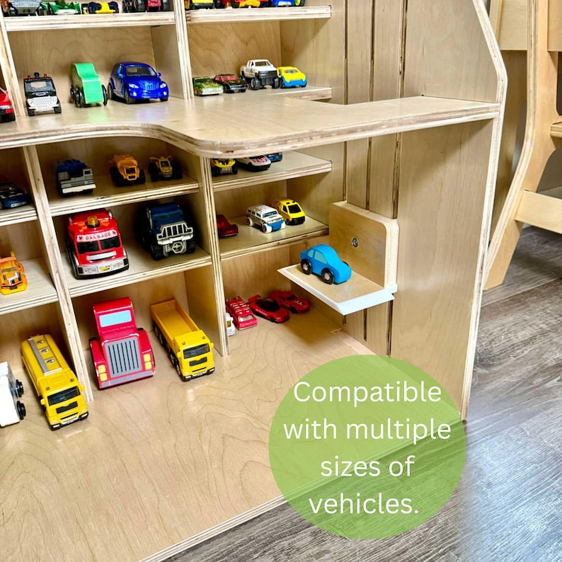 May include: A wooden toy car display shelf filled with various toy vehicles. The shelf is light-colored with multiple compartments and a small shelf. The image includes a variety of toy cars, trucks, and emergency vehicles in different colors.
