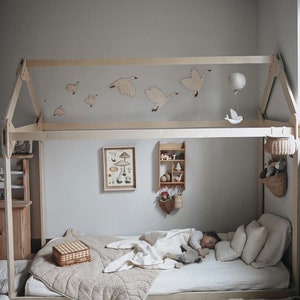 May include: A wooden bed frame with a house-shaped canopy, featuring a white and beige quilt, a wicker basket, and wooden bird decorations on the ceiling.
