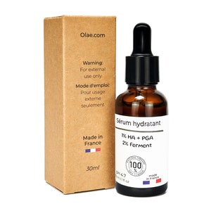 May include: A brown cardboard box with a white label that says "Olae.com" and a description of the product inside. The product is a clear glass bottle with a black dropper and a white label that says "Sérum hydratant 1% HA + PGA 2% Ferment". The bottle is sitting on a white background.