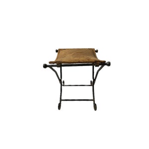 May include: A black metal stool with a brown leather seat. The stool has a simple design with four legs and a rectangular seat.