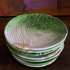 Peut inclure: Une pile d'assiettes en céramique avec un motif de feuille de laitue. Les assiettes sont blanches et vertes, avec une surface texturée qui imite les nervures d'une feuille de laitue. Les assiettes sont empilées les unes sur les autres.