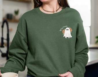 May include: A green sweatshirt with a white ghost and the text "Spooky Season" in white. The ghost is surrounded by orange flowers.