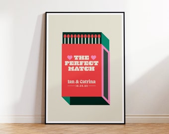 May include: A framed print with a matchbox design. The red matchbox has the text "THE PERFECT MATCH" and the names "Ian & Catrina" with the date "19.05.23". The match heads are red, and the box has green and pink accents. The print is in a black frame.