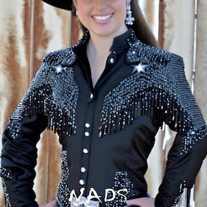 May include: A black satin shirt with a beaded design and fringe. The shirt has a button-up front and long sleeves. The shirt is decorated with rhinestones and the word "NADS" is visible on the front.