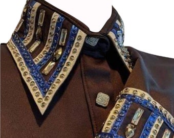 Op de afbeelding: Een bruin shirt met een witte en blauwe, versierde kraag en manchetten. De kraag heeft een puntige vorm en de manchetten een geometrisch patroon. Het shirt heeft het woord "NADS" op de onderkant.