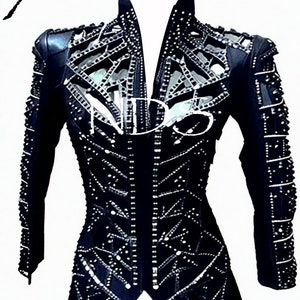 May include: A black leather jacket with a geometric design and rhinestones. The jacket has a stand-up collar and long sleeves.