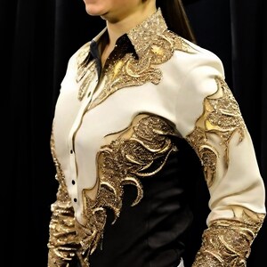 May include: A white and black long-sleeved shirt with gold embroidery. The shirt has a button-up front and a pointed collar.
