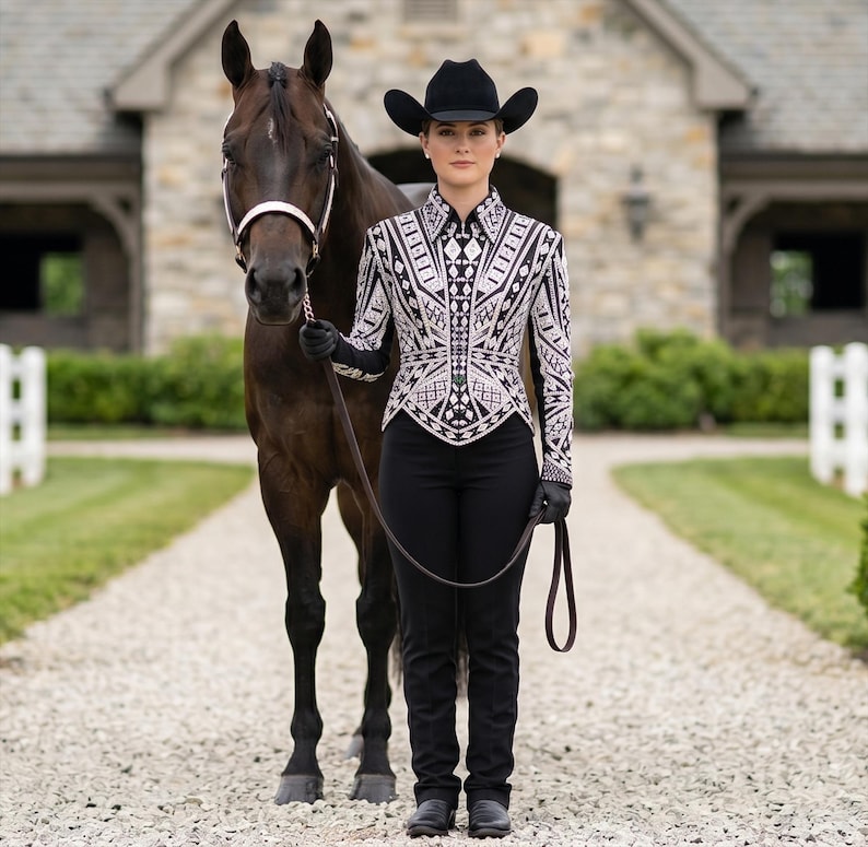 May include: A dark brown horse with a white halter stands next to a person wearing a black cowboy hat, black gloves, black trousers, and a long-sleeved shirt featuring a detailed white and black geometric pattern with a structured, pointed hem.