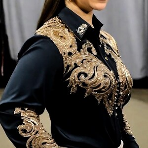 May include: A black long-sleeved shirt with gold embroidery on the front and sleeves. The shirt has a collar and button closure.