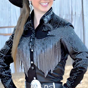 May include: A black long-sleeved shirt with silver fringe and rhinestones. The shirt has a button-up front and a pointed collar.