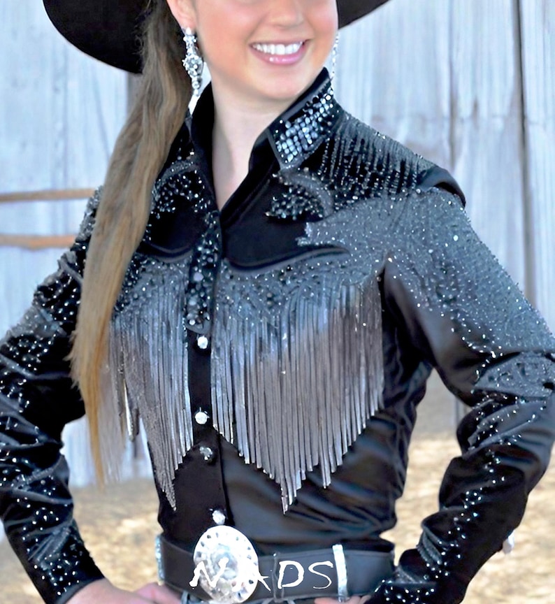 May include: A black long-sleeved shirt with silver fringe and rhinestones. The shirt has a button-up front and a pointed collar.