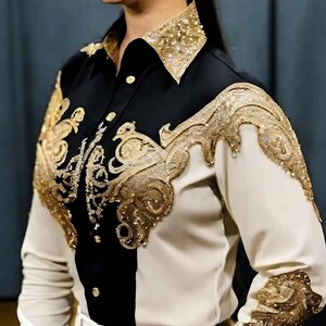 May include: A white and black long-sleeved shirt with gold embroidery. The shirt has a collar and a button-up front. The embroidery is in a floral pattern and covers the shoulders and sleeves.