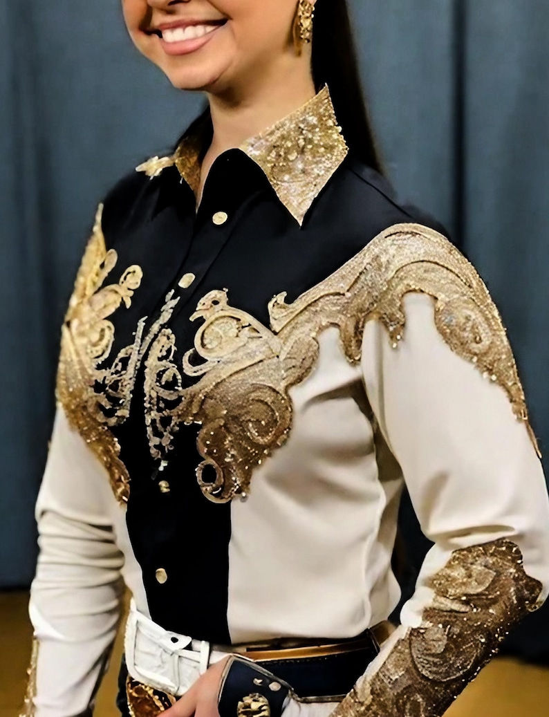May include: A white and black long-sleeved shirt with gold embroidery. The shirt has a collar and a button-up front. The embroidery is in a floral pattern and covers the shoulders and sleeves.