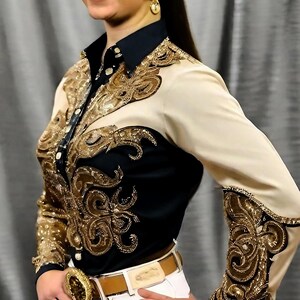 May include: A black and beige long-sleeved shirt with gold embroidery. The shirt has a button-up collar and a brown belt.