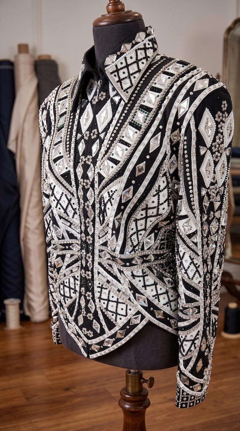 May include: A black long-sleeve jacket featuring an intricate pattern of white fabric panels, silver-toned metallic accents, and numerous clear, diamond-shaped crystals arranged in geometric designs across the front and sleeves.