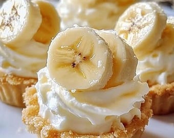 May include: Three mini tarts with a creamy white filling topped with sliced banana. The tarts have a golden brown crust.