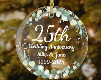 Könnte beinhalten: Ein klarer, runder Ornament mit dem Text "25. Hochzeitstag Mike & Jane 1999-2024" in Weiß. Das Ornament ist mit einem grün-weißen Blumendesign verziert und wird von einem goldenen Band gehalten.