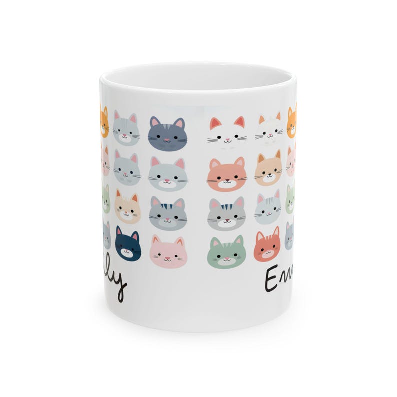May include: White ceramic mug decorated with a repeating pattern of colorful cat faces. The cat faces are in various colors, including orange, gray, pink, and blue. The names "Emily" and "Lily" are written on the mug in black script.