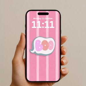 Può includere: Uno smartphone che mostra una schermata di blocco con uno sfondo a righe verticali rosa e bianche. Lo schermo mostra la data lunedì 11 ottobre e l'ora 11:11 in testo bianco. Un fumetto con la parola BOO è centrato sullo schermo.